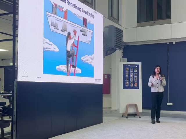 Shirley He presenting a slide of a woman climbing a red ladder through a glass ceiling